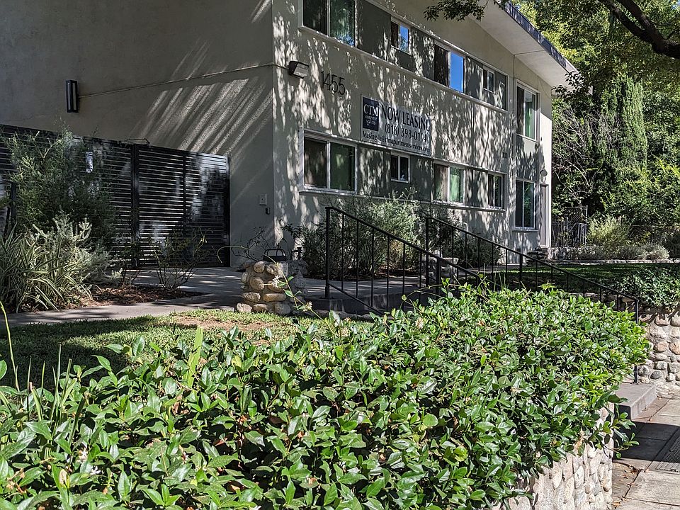 Sidewalk view of stone wall garden beds and mature shade trees in front of Los Robles Apartments in Pasadena, California.