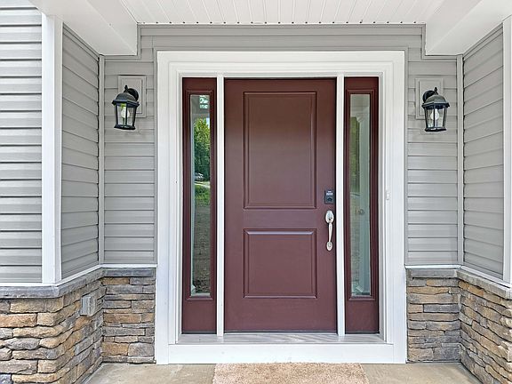 Stylish front entrance with maroon door, flanked by sidelights, gray siding, and stone accents, illu