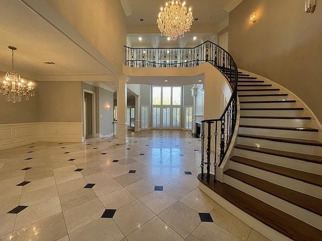 Foyer featuring a chandelier, a decorative wall, a wainscoted wall, ornamental molding, and stairway