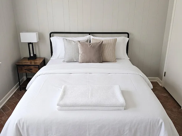 Furnished bedroom with a full-size bed, nightstand and lamp, plus a paneled accent wall for a polished look.