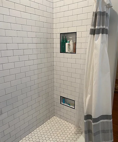 Renovated bathroom with new plumbing and tile shower with hand shower spray and storage for accessories