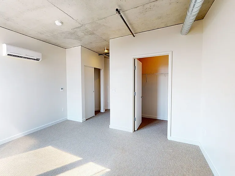 Spacious apartment bedroom with large closet and plush carpet flooring.