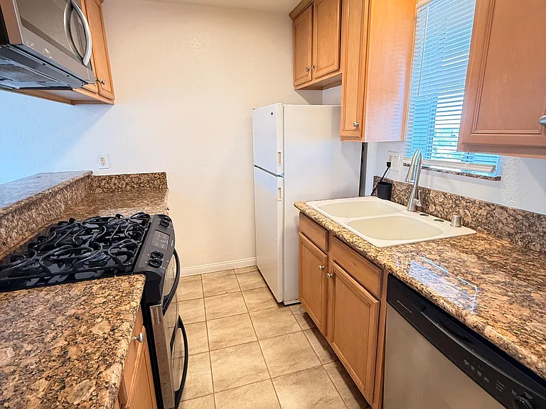 Galley kitchen with gas stove, oven, refrigerator, microwave and dishwasher