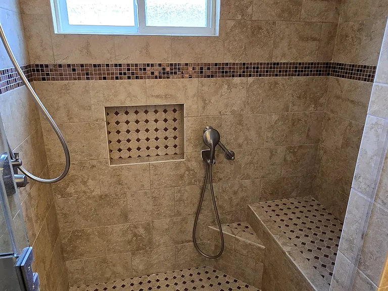 Shower features recessed soap niche and separate shower sprayer arm accessible from shower seat