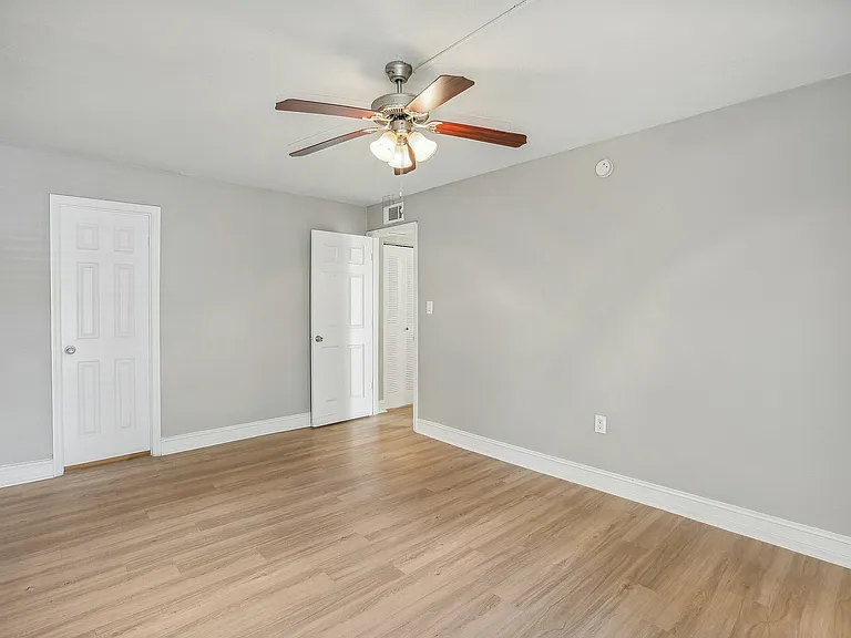 Bright, spacious bedroom with sleek hardwood floors and fresh gray walls, featuring a ceiling fan and ample natural light.