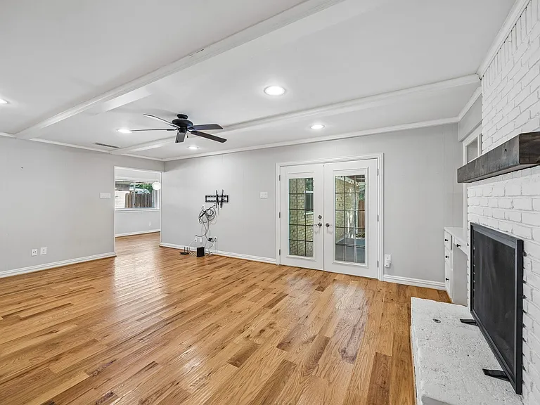 Living area featuring wood-finish flooring, a white-painted brick fireplace with a wood mantel, and white French doors