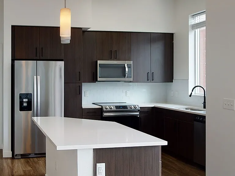 Apartment kitchen with stainless steel appliances, quartz countertops and wood-style flooring.