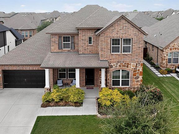 View of front facade with a shingled roof, an attached garage, brick siding, stone siding, and driveway
