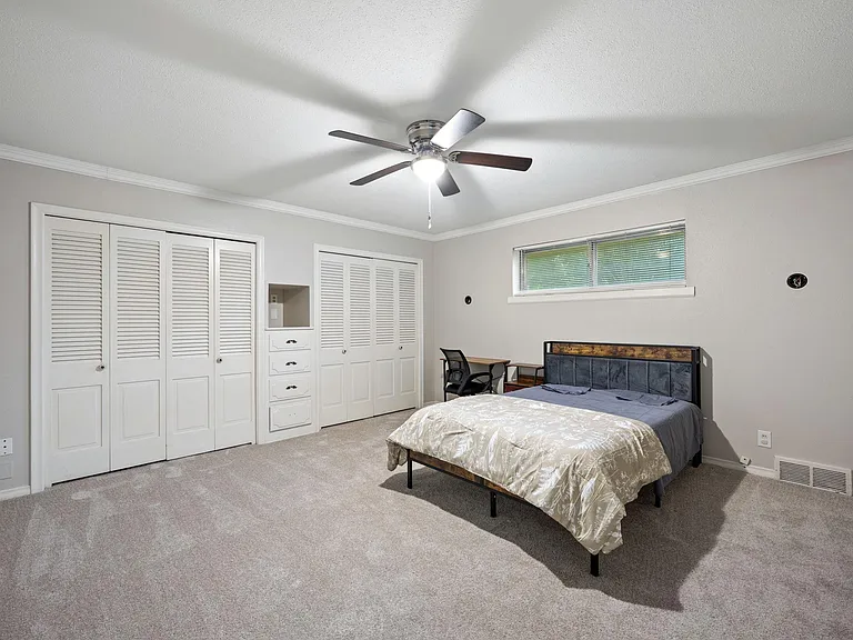 Spacious bedroom with a ceiling fan, large double closets, and a window with blinds plus a small desk area.