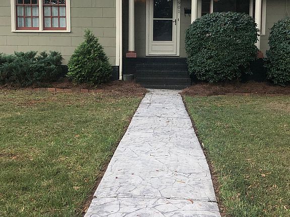 Stamped concrete sidewalk leading to front porch with large picture window and a porch swing