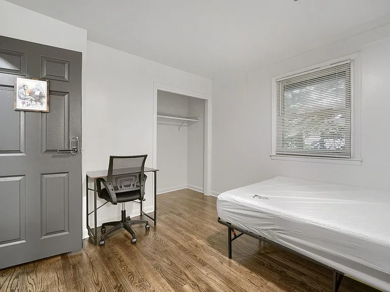 Private bedroom with hardwood floors, a window with blinds, open closet storage, and a dedicated desk workspace.