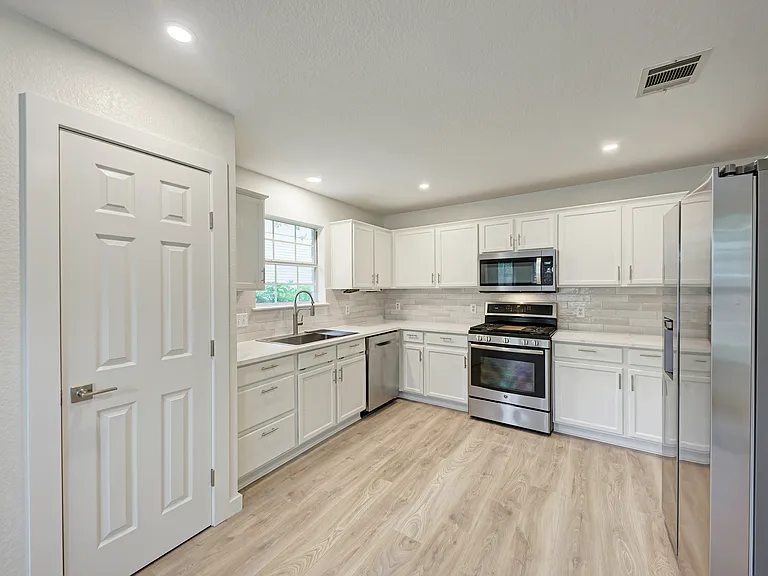 Open-concept kitchen featuring white cabinetry, white quartz countertops, stainless steel appliances
