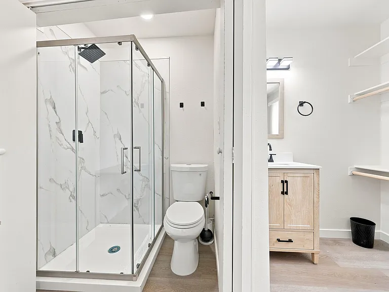 Updated bathroom with a glass-enclosed shower, rain showerhead, and vanity storage with contemporary fixtures.