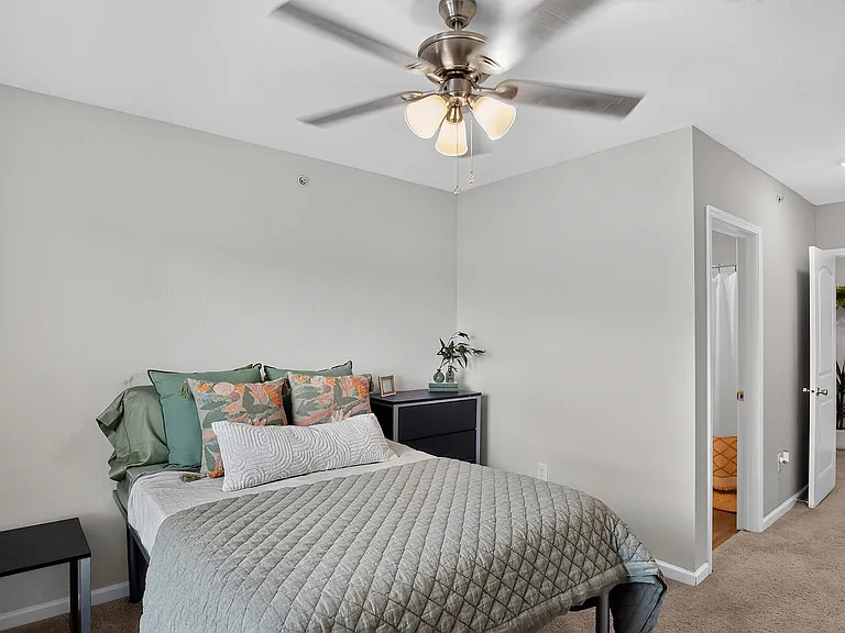Cozy bedroom featuring elegant decor, plush bedding, and modern ceiling fan, with en-suite bathroom access.