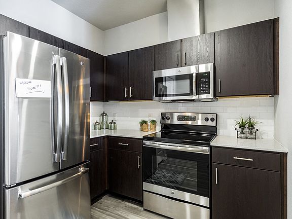 Kitchen with dark cabiets, stainless steel appliances, quartz countertops, and subway tile backsplash