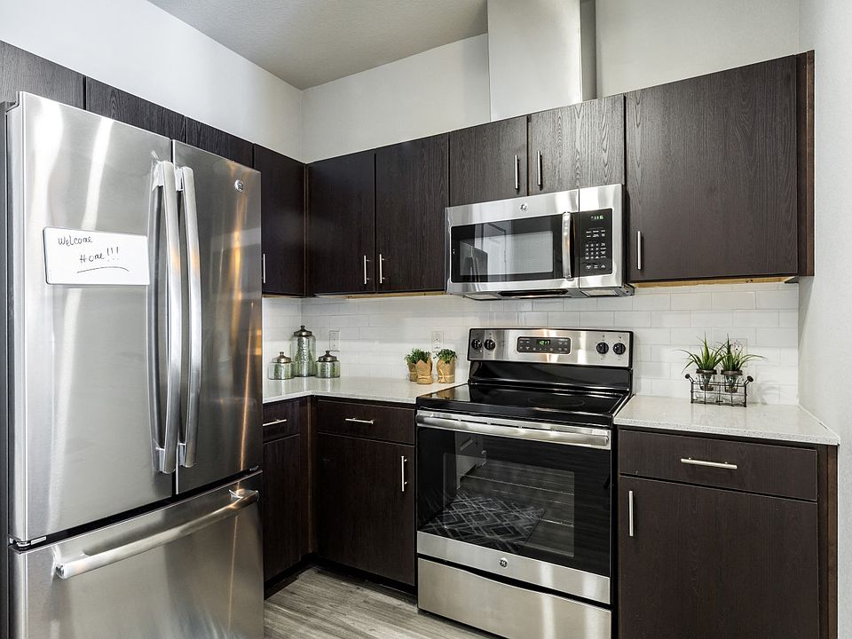 Kitchen with dark cabiets, stainless steel appliances, quartz countertops, and subway tile backsplash