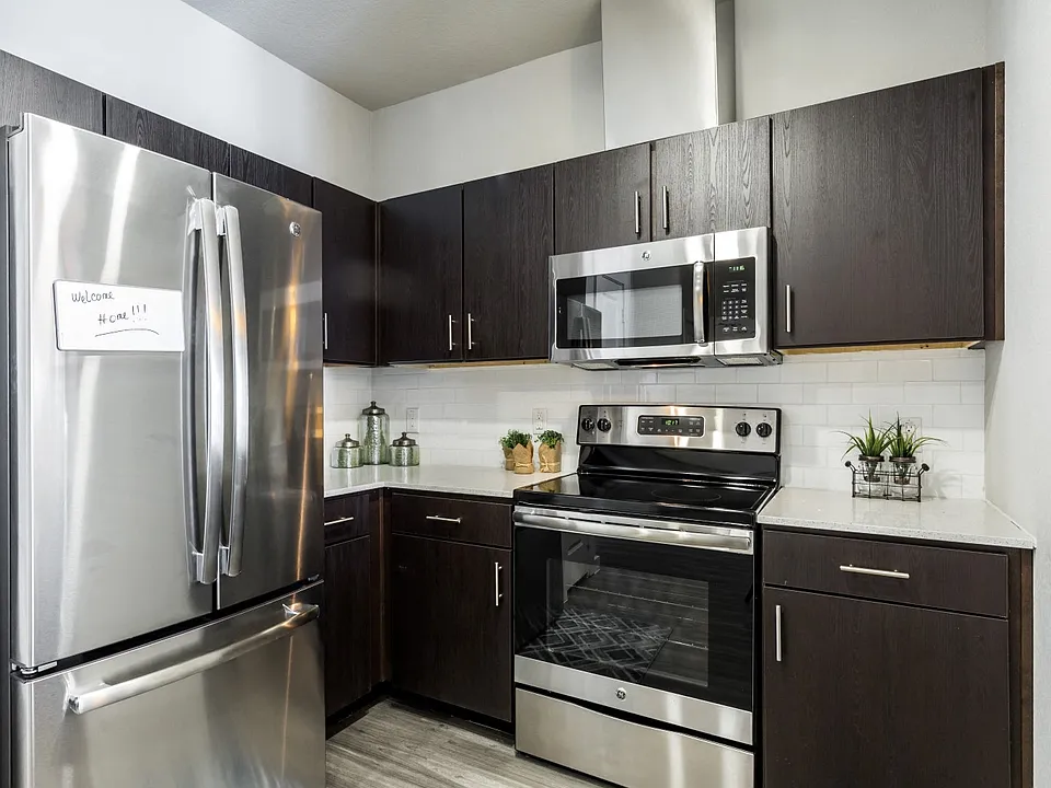 Kitchen with dark cabiets, stainless steel appliances, quartz countertops, and subway tile backsplash