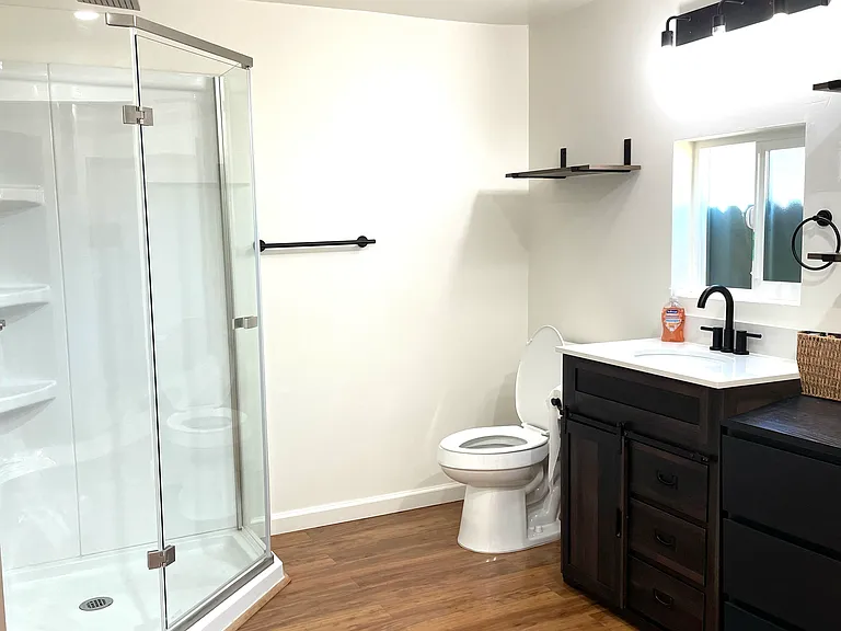 Oversized bathroom with a small cabinet with sink, two dressers filled with drawers (matching taller one not shown in photo), and a small, electric water heater.