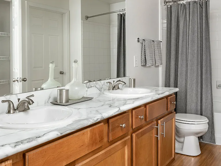 Apartment bathroom with wood-style flooring and marble-style countertops (shown here). Quartz-style countertops are available in select homes.