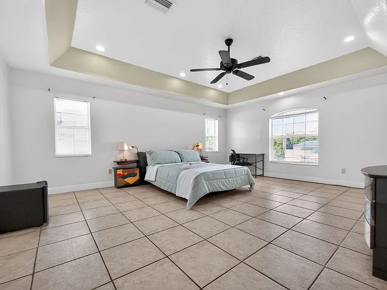 Spacious bedroom with tray ceiling, recessed lighting, ceiling fan, and large windows plus a dedicated desk area.