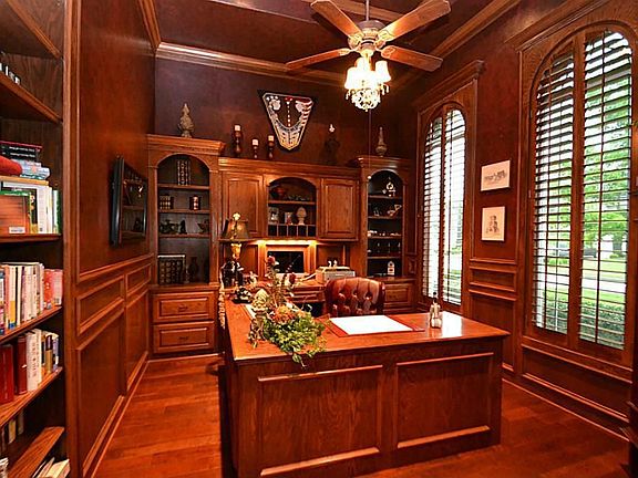 French doors with transom glass above  opens to the stately study accented by hardwood floors, blocked paneling, built-ins with bookshelves, ceiling fan with light fixture, triple crown molding, recessed lighting and hand stained plantation shutters.