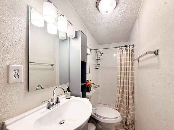 Full bathroom with tub/shower combo, vanity with mirror, and added storage shelving for everyday essentials.