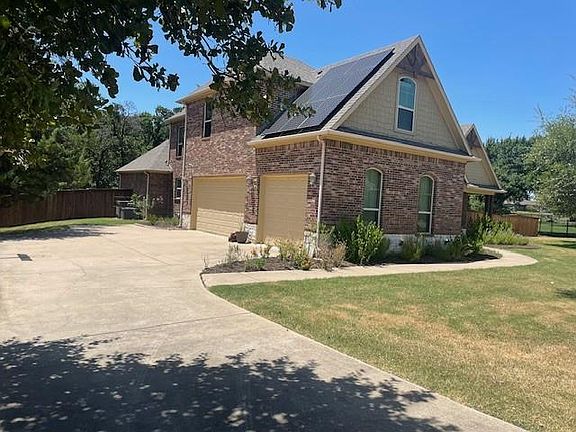 View of home''s exterior featuring roof mounted solar panels, brick siding, driveway, a garage, and roof with shingles