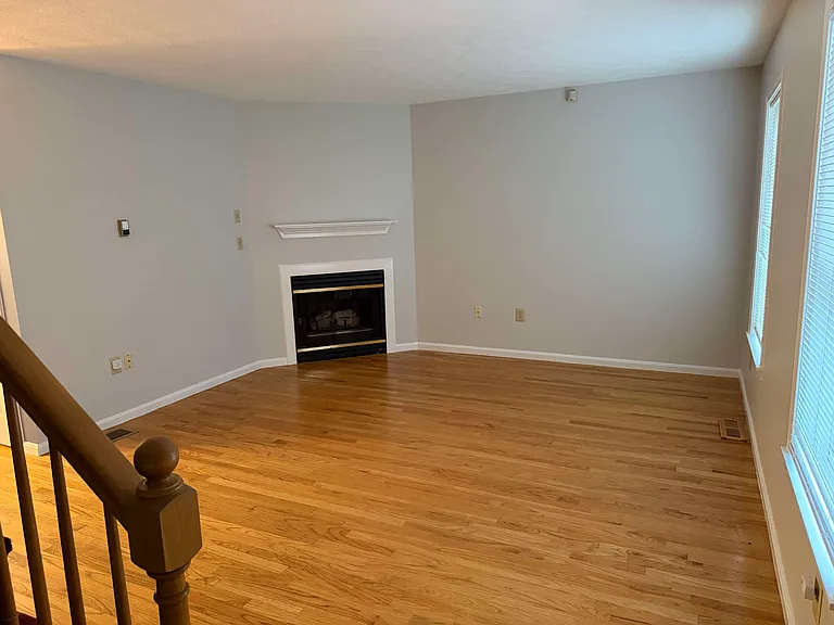 Large living room, gas fireplace with mantel and two large windows overlooking the manicured grounds