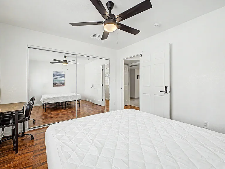 Spacious bedroom with ceiling fan, wood-look flooring, mirrored closet doors, and a dedicated desk area for work or study.