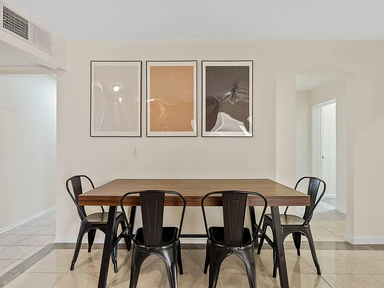 Dedicated dining area with a large table for four, tile flooring, and wall space for artwork near adjacent rooms.