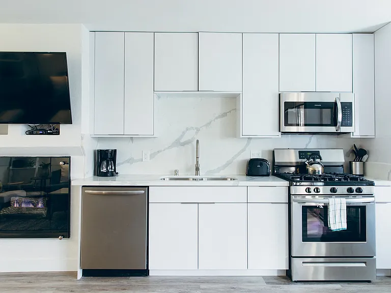 Kitchen with stainless steel dishwasher, gas range, micro hood microwave, single kitchen sink, backsplash and countertops, white kitchen cabinets, cozy fireplace on the left