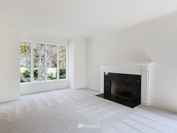 Formal living room showcases large windows and marble-faced wood-burning fireplace with formal mantle.