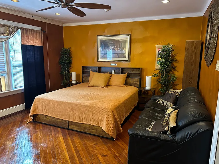 Furnished bedroom with hardwood floors, a ceiling fan, bedside lighting, and a large window for natural light.
