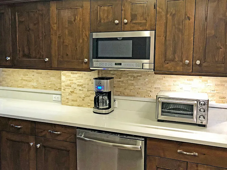 The kitchen has a longer counter with coffee maker and toaster oven. The upper cabinets contain dishware and glassware, and below is the cookware.