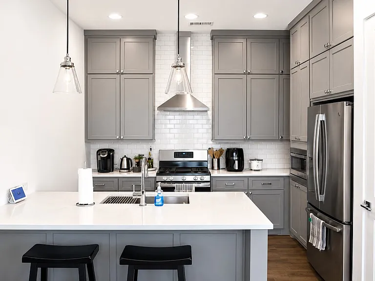 Kitchen featuring an island with white countertop, gray cabinetry, stainless steel appliances, and subway tile backsplash