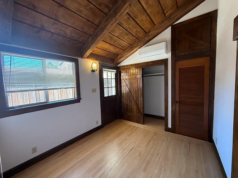 Bedroom #4 features wooden valuted ceiling, one window, patio door to backyard and 2 closets with a split AC cooling unit.