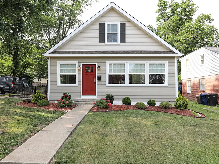 Spacious front exterior of home with red front door and landscaped yard.