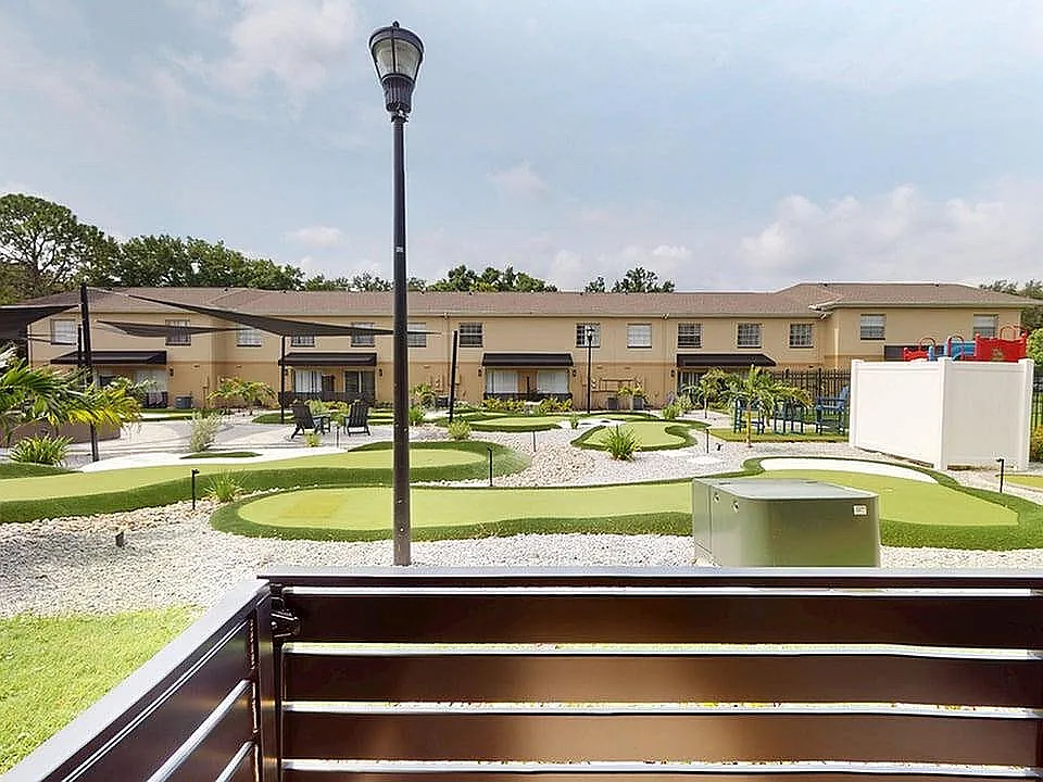 Charming apartment view showcasing a beautifully landscaped courtyard with lush greenery, a mini-golf area, and modern play structures, perfect for outdoor relaxation.