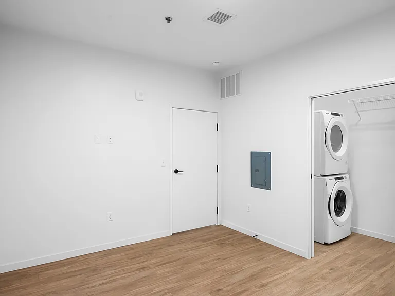 Bright laundry area featuring a modern stacked washer and dryer with sleek wood flooring and a minimalist white interior design. Bright laundry area featuring a modern stacked washer and dryer with sleek wood flooring and a minimalist white interior desig