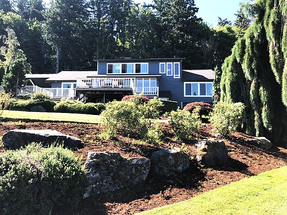 Bay side of the 3 level house from the lower lawn, landscaped with rose bushes, hydrangeas, evergreens and fruit trees.
