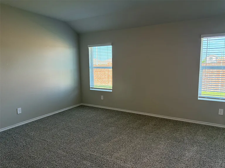 Carpeted room with vaulted ceiling and two windows featuring horizontal blinds