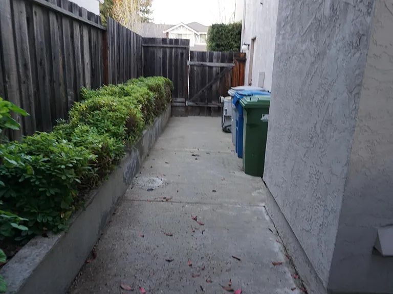 left side gate with space for garbage bins and ac unit seen, next to AC unit entry door to garage