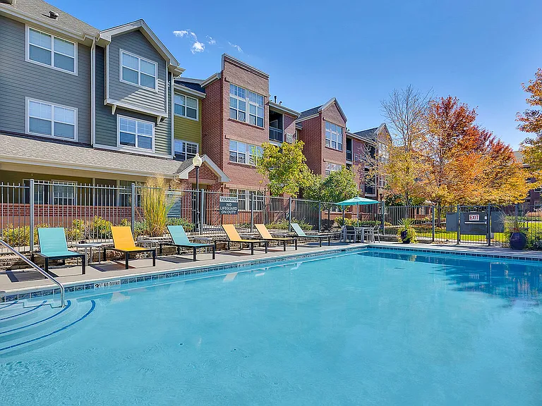 Charming apartment complex with a sparkling outdoor pool, colorful lounge chairs, and beautifully landscaped surroundings.