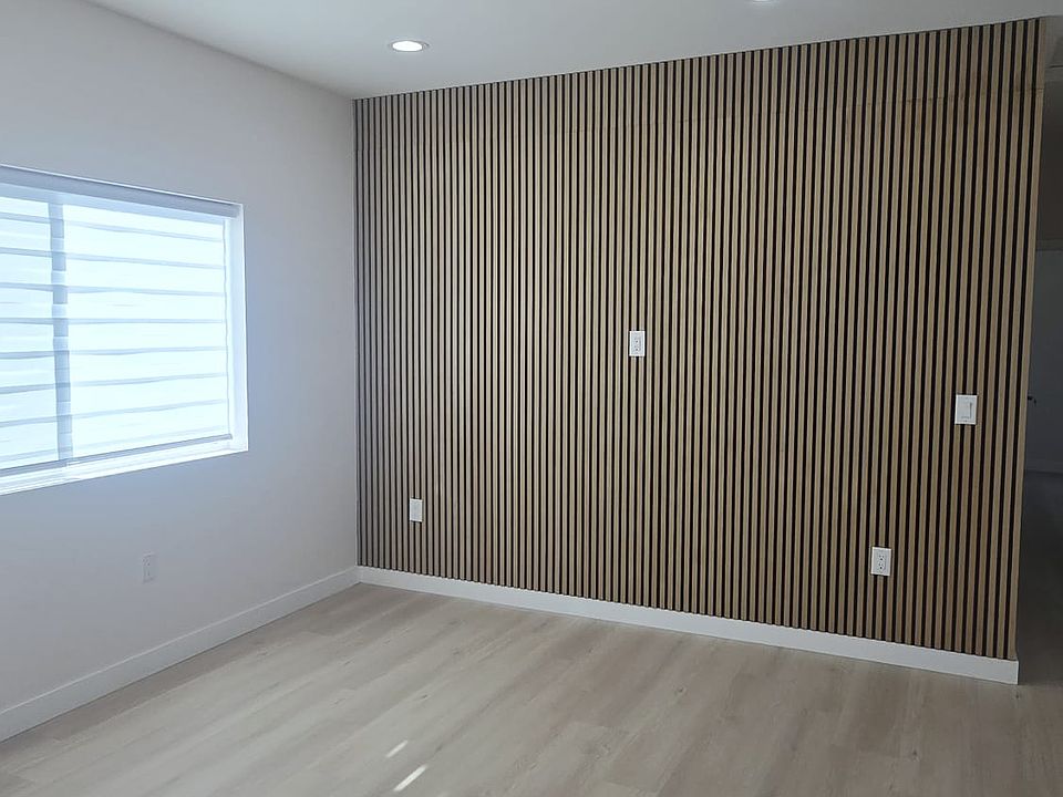 Modern living area with stylish wall panel accent, bright dimmable LED recessed lighting, and large window for natural light. Features retractable window blinds and clean, contemporary design_perfect for relaxing or movie nights.