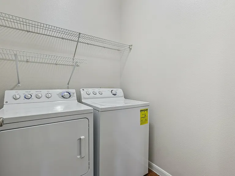 Modern laundry room featuring sleek washer and dryer units with ample storage shelving above. Modern laundry room featuring sleek washer and dryer units with ample storage shelving above.