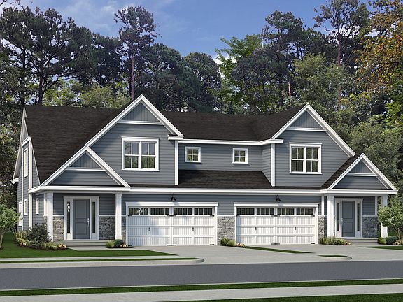 A modern two-story, blue-gray duplex with white trim, featuring two front-facing garages, situated i
