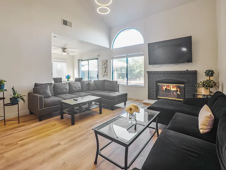 Unwind in the spacious living room featuring soaring ceilings, a modern chandelier, plush seating, a smart TV, and scenic views of the beautifully landscaped backyard.