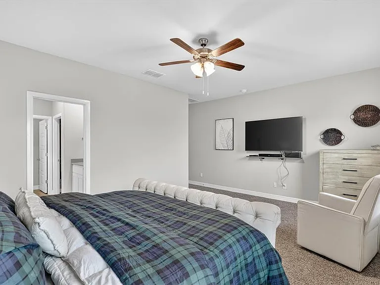 Spacious bedroom featuring light neutral wall tones, carpeted flooring, and a ceiling fan with integrated lighting