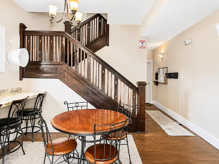Dining area with a round table plus a granite breakfast bar, set beside a wide staircase and open hallway for easy flow.