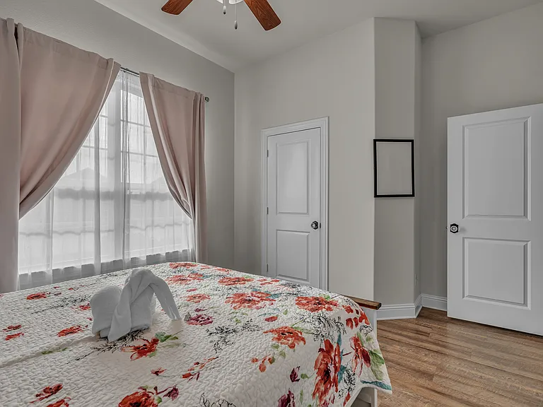 2nd guestroom in front of the home with a large closet, a queen bed, a pull-out drawer under, a side table, a lamp, and a ceiling fan.